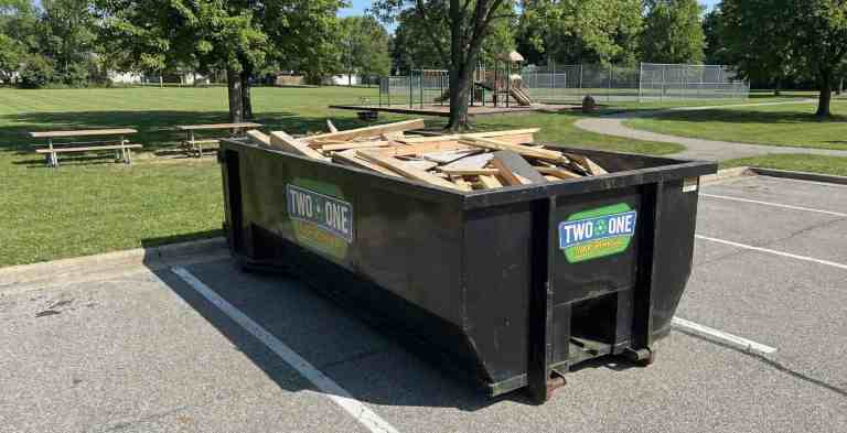 Black dumpster with "Two in One Junk Removal" logo in a parking lot.