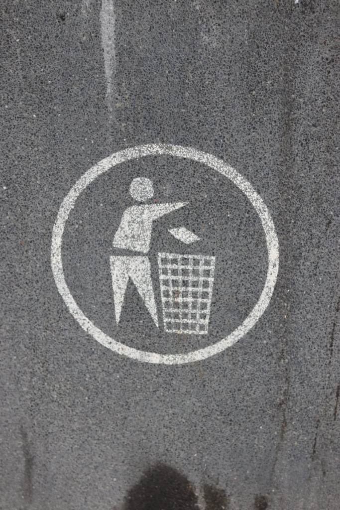 Icon showing person throwing trash into a bin on urban pavement.