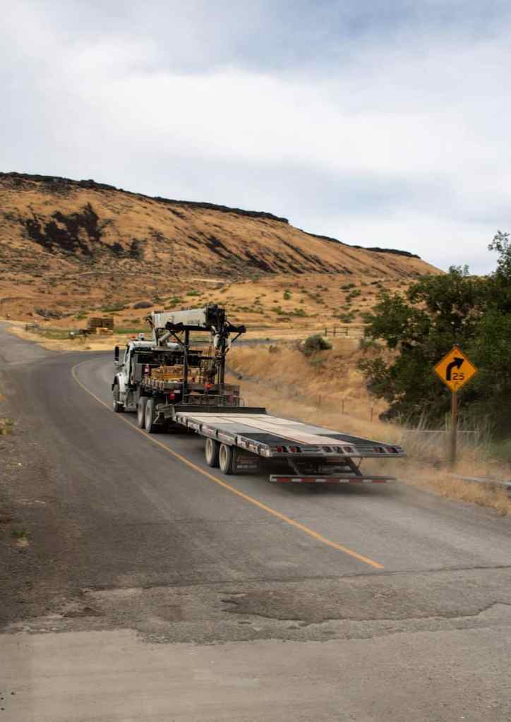 A semi truck driving down a road next to a hill