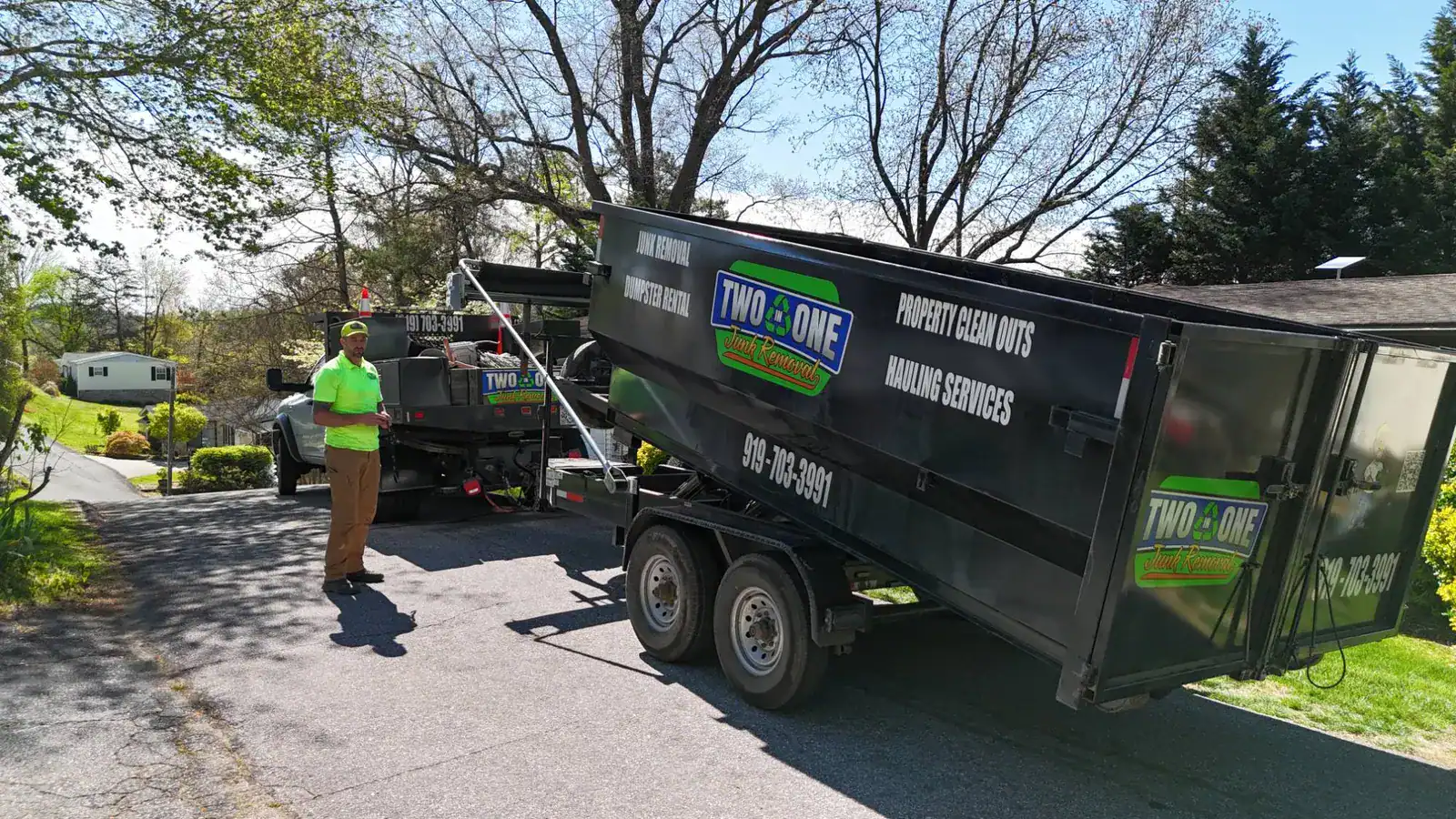 Two in One Junk Removal crew member standing beside the company dump trailer